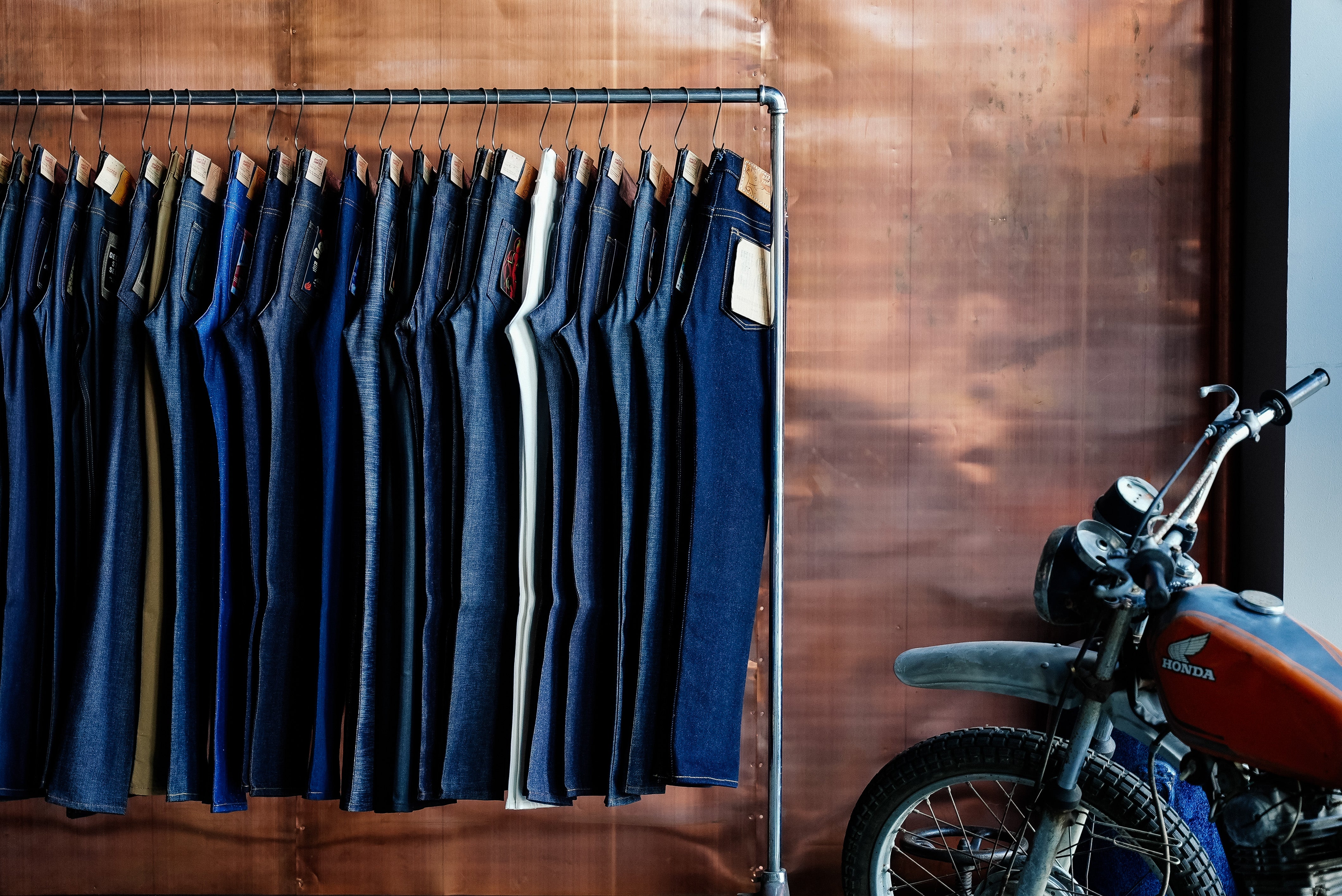 Rack of blue denim jeans against a wooden wall with a motorcycle in the foreground.