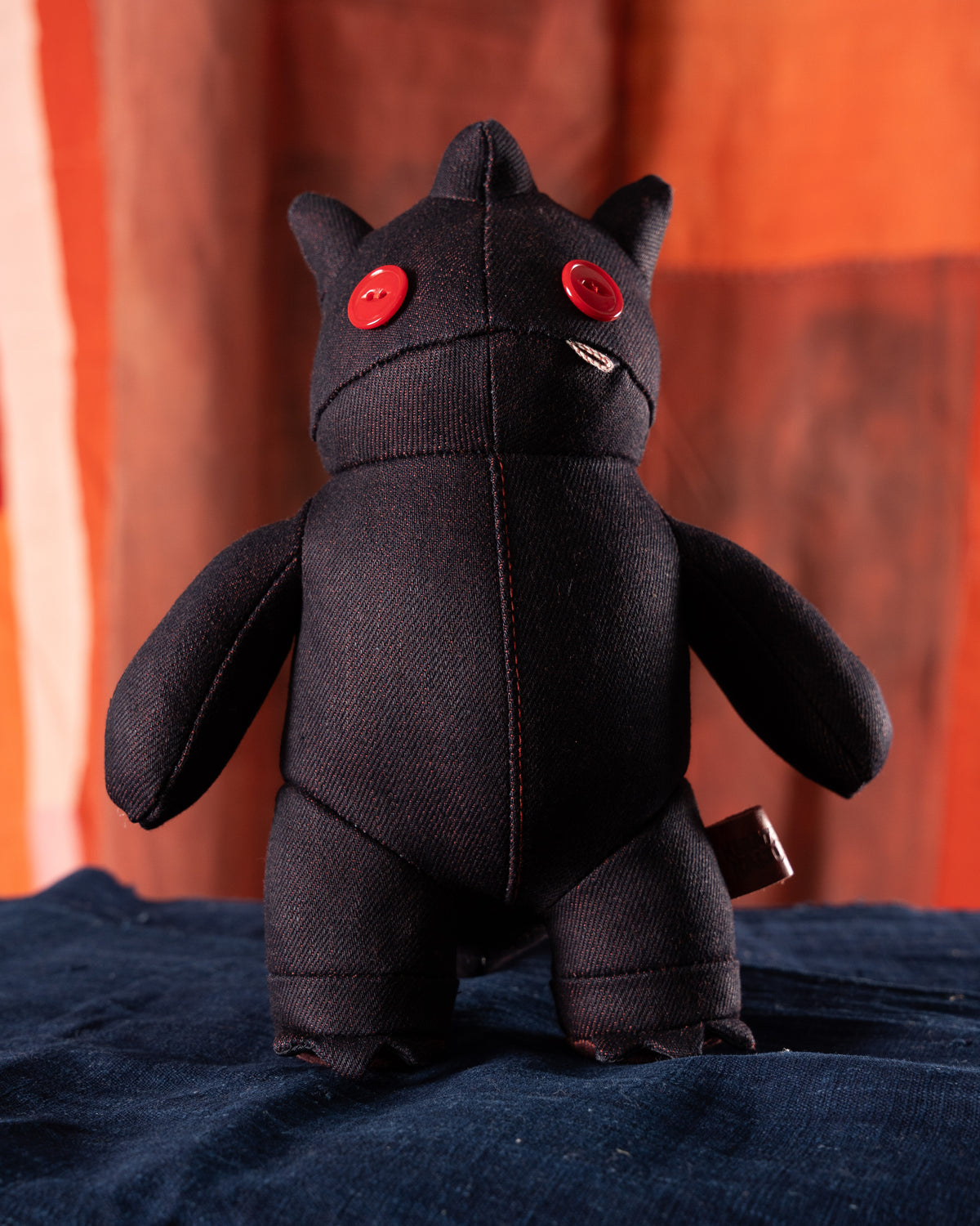 Black plush toy with red buttons on a blue surface with an orange curtain background